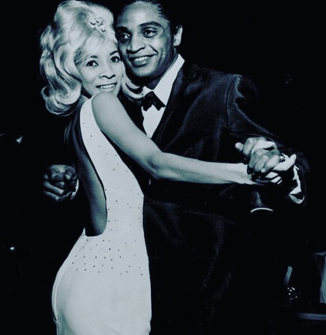 Berry Gordy in a black formal suit dancing with Ray Singeton in a white bodycon.